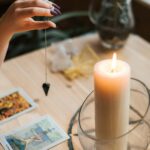 Crop soothsayer with talisman and tarot cards near glowing candle