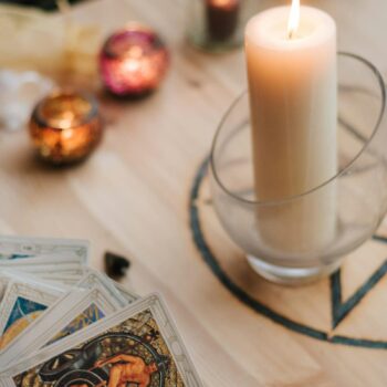 From above of crop anonymous fortune teller with set of tarot cards near burning candles during divination process