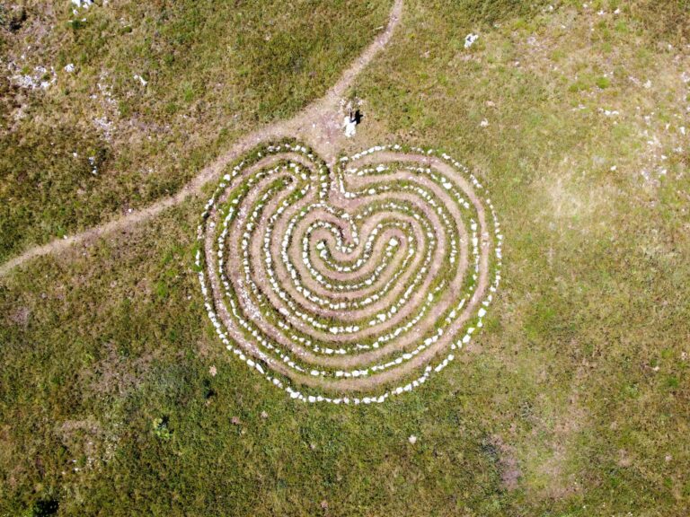 A heart-shaped labyrinth outlined with stones in a grassy field, captured from above.