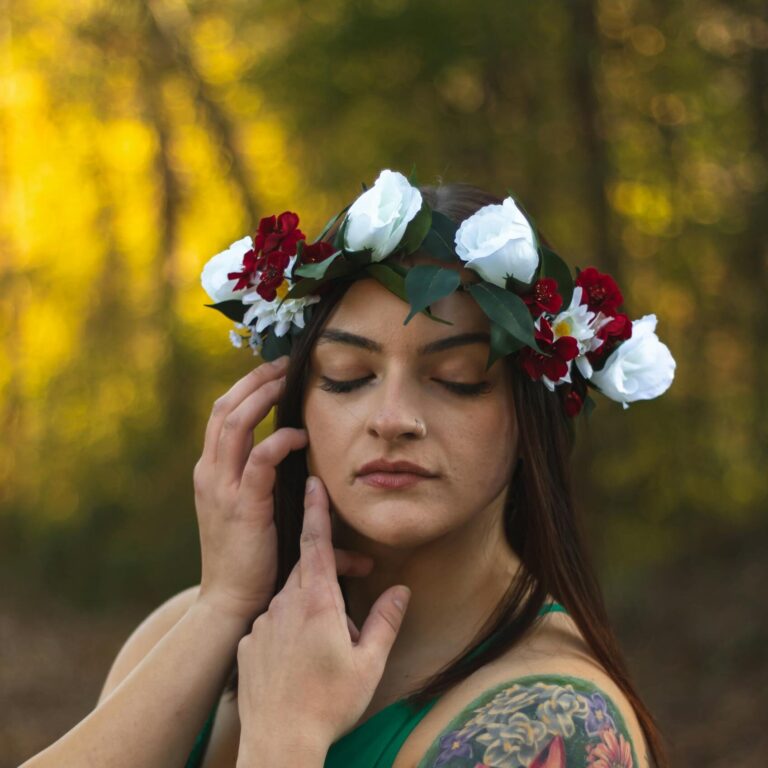 Woman with floral crown and colorful arm tattoo in a serene outdoor setting, showcasing nature and art.
