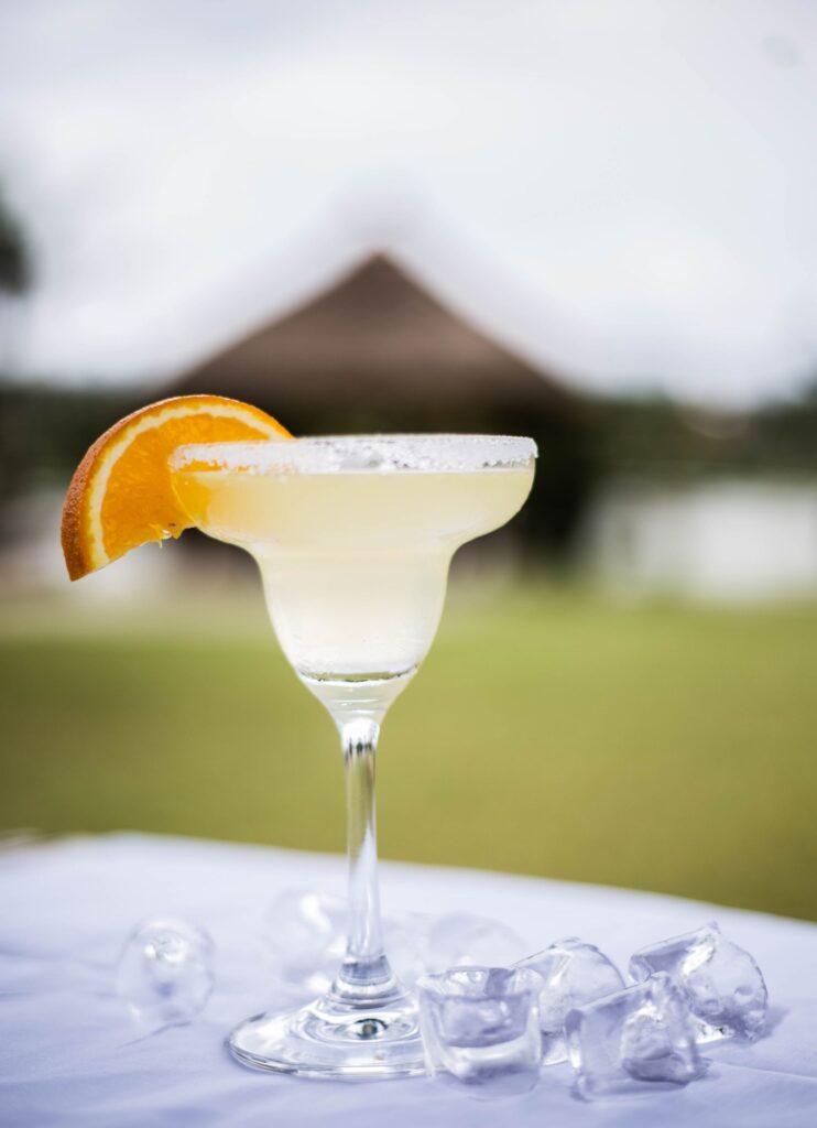 A chilled margarita garnished with orange slice on a sunny day in an outdoor setting.